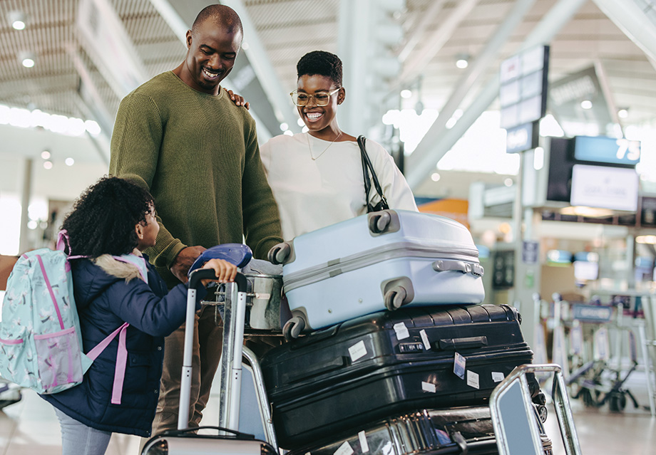 Happy parents and young daughter with luggage standing at airport. African family of three at airport terminal waiting for flight.