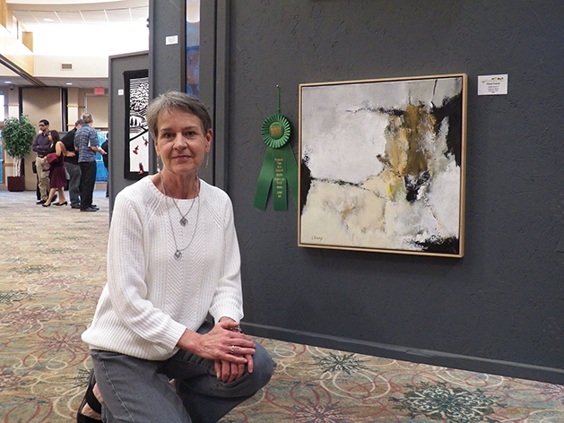Artist next to award-winning painting at Plymouth's Primavera art exhibition.