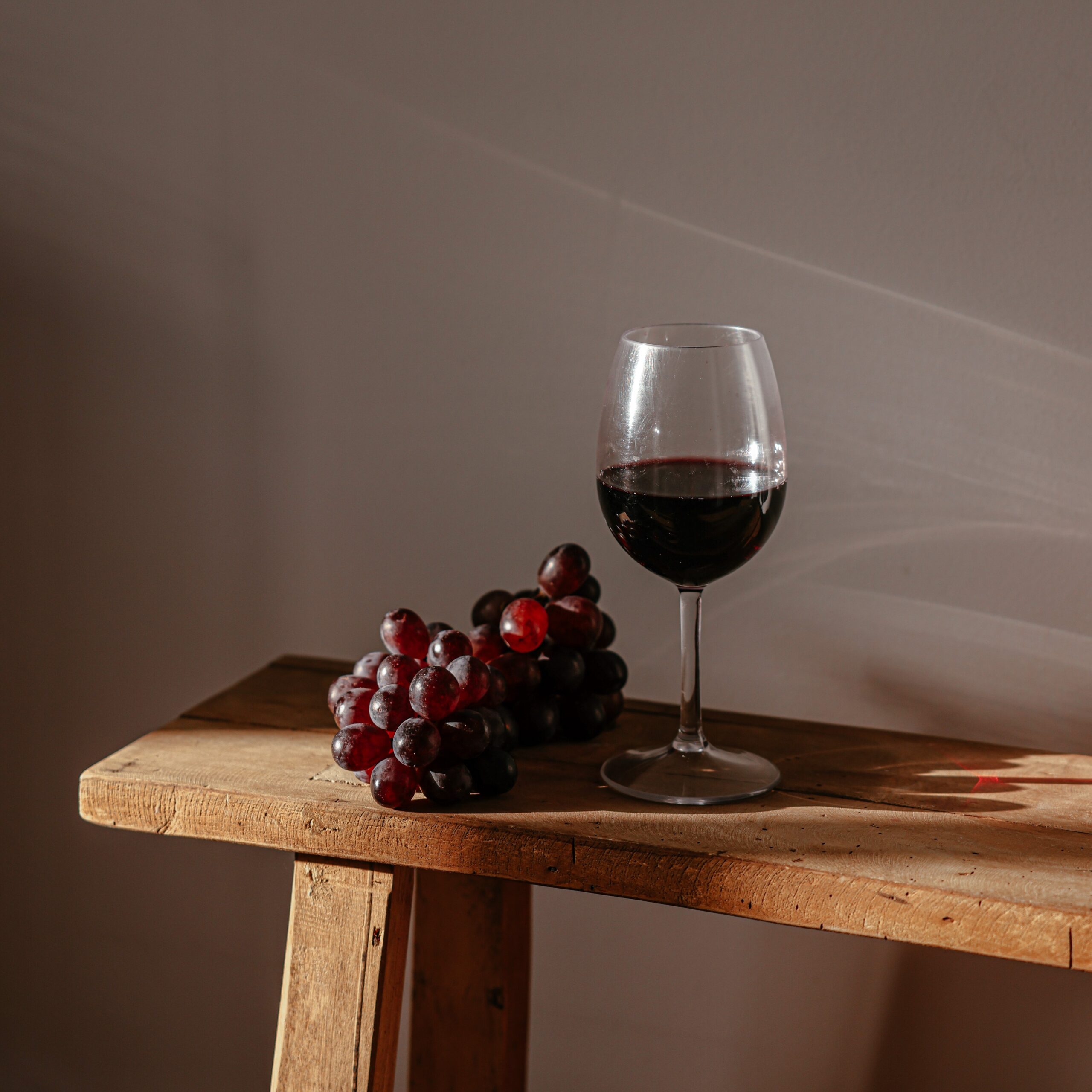 Glass of red wine next to grapes on a wooden bench.