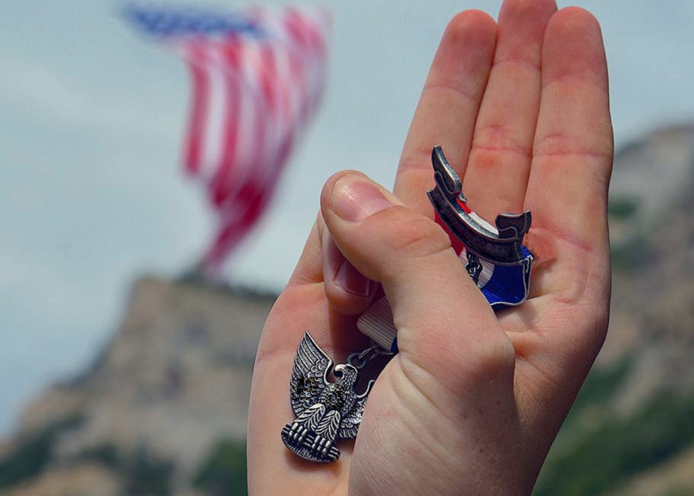 A hand holding the Eagle Scout badge makes the Boy Scouts' salute.