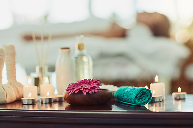 A woman relaxes at a spa. In the foregroun, a towel, candles and various other wellness items sit on a table.