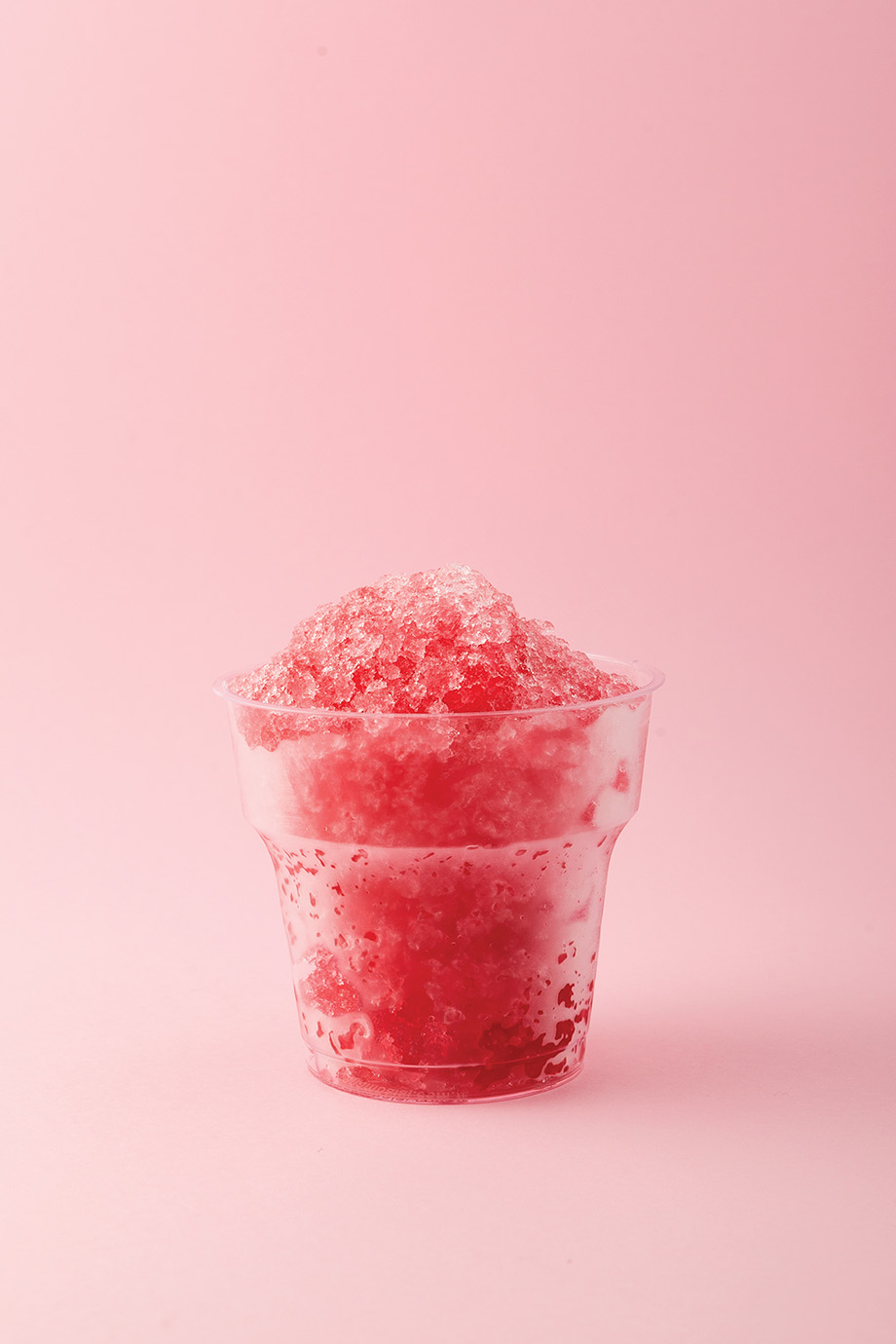 Slushie or Slush - drink on pink background. Fruit shaved ice in disposable plastic cup. Take away food. Refreshing summer drink. Vertical orientation, copy space.