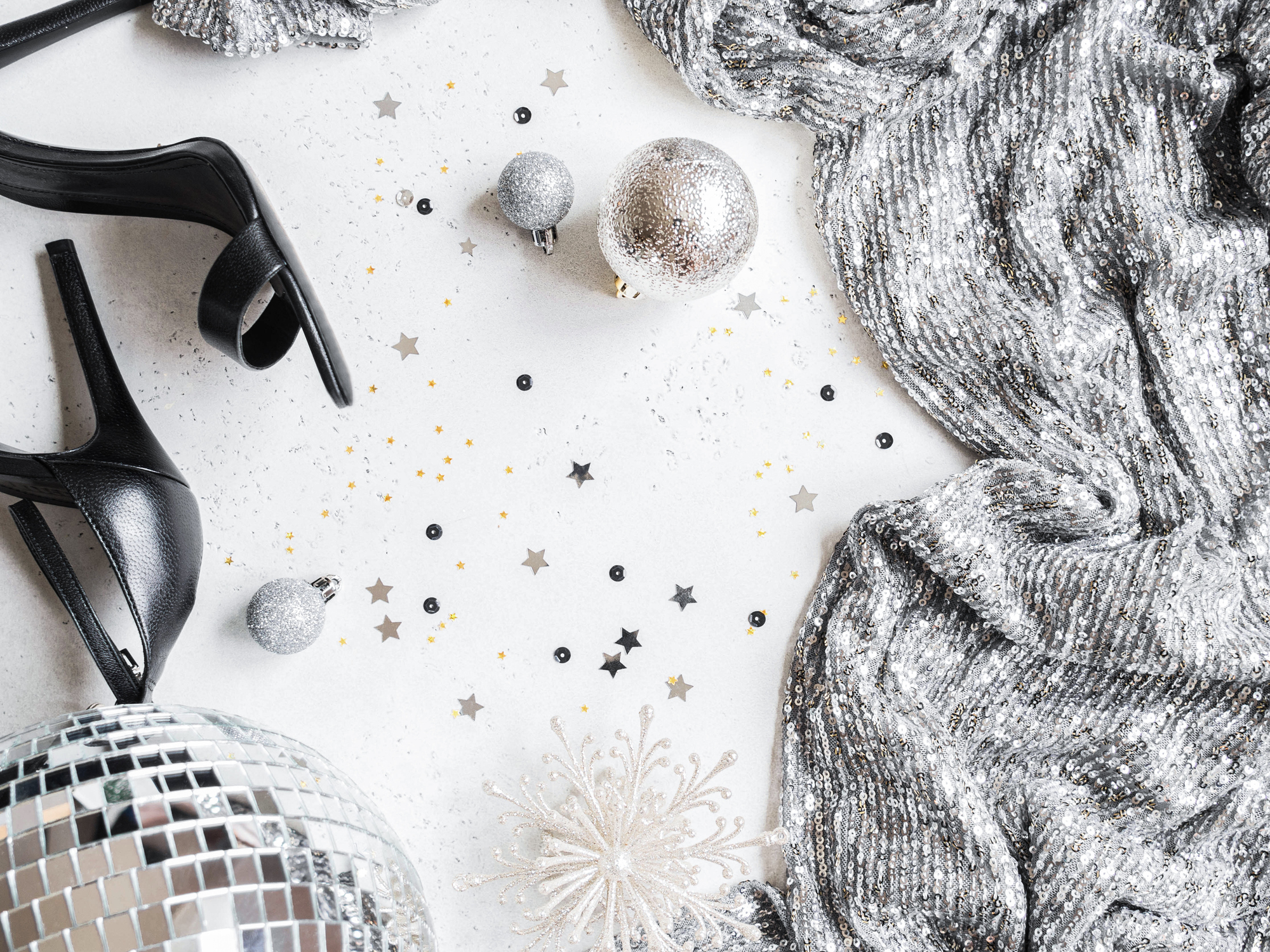 Flat lay of Christmas party disco ball, black shoes, dress, season decoration on white background. Top view. Copy space