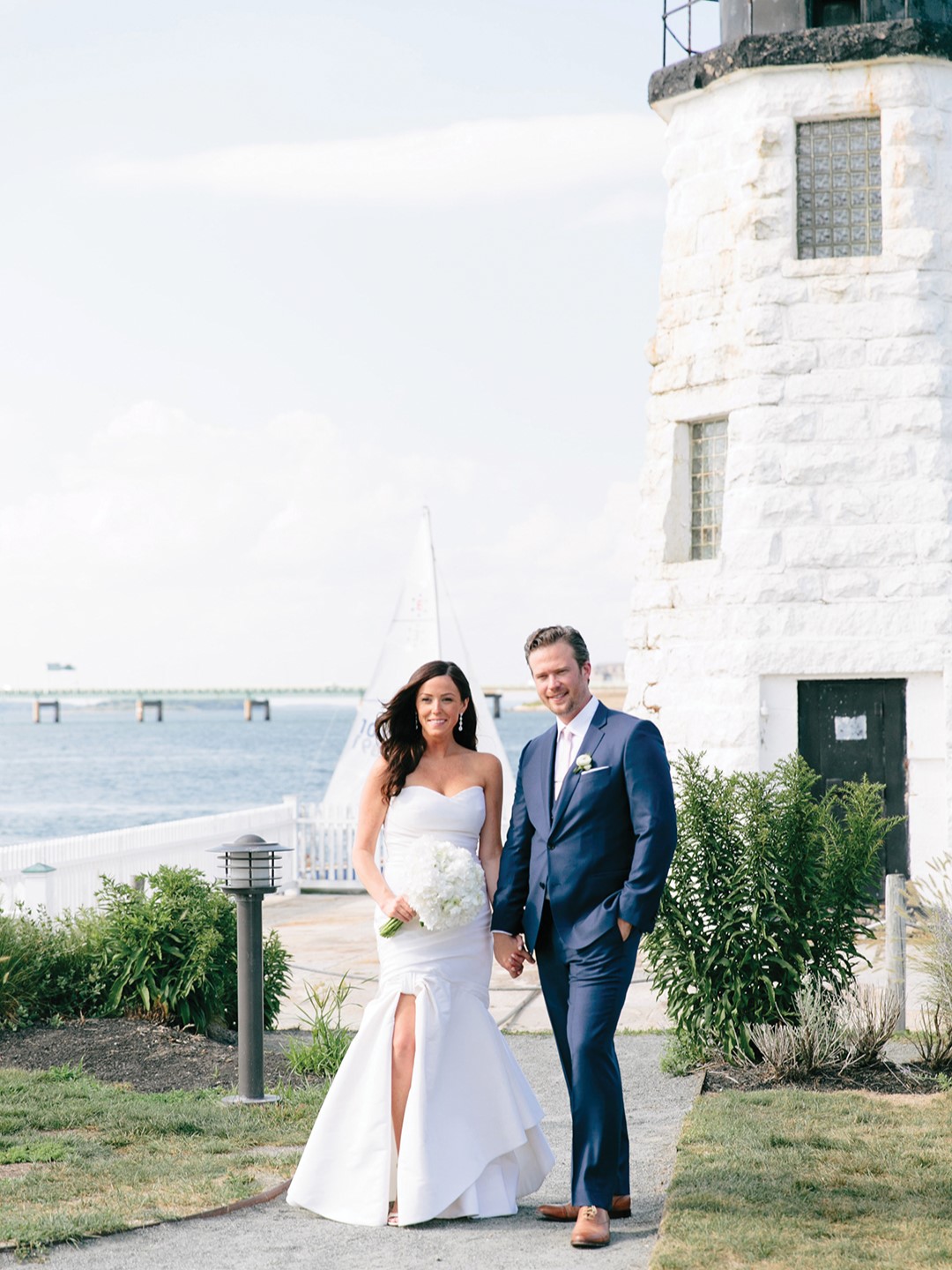 Andrea and Chris Nelson stand in front of the Newport Harbor Light, an iconic landmark on Goat Island in Newport, Rhode Island, where they hosted their wedding reception.