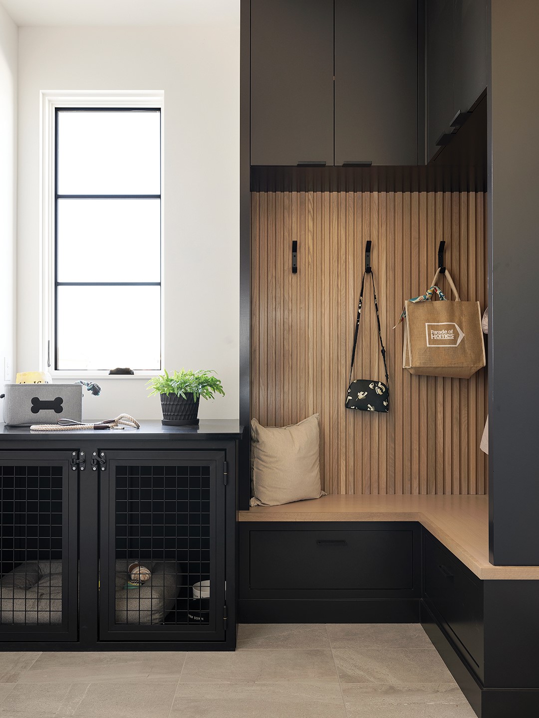 This specific mudroom pulls double duty as a dedicated dog house. Dark cabinets in Sherwin-Williams Black Magic, which match the kennel, are accented by durable white oak wood slat.