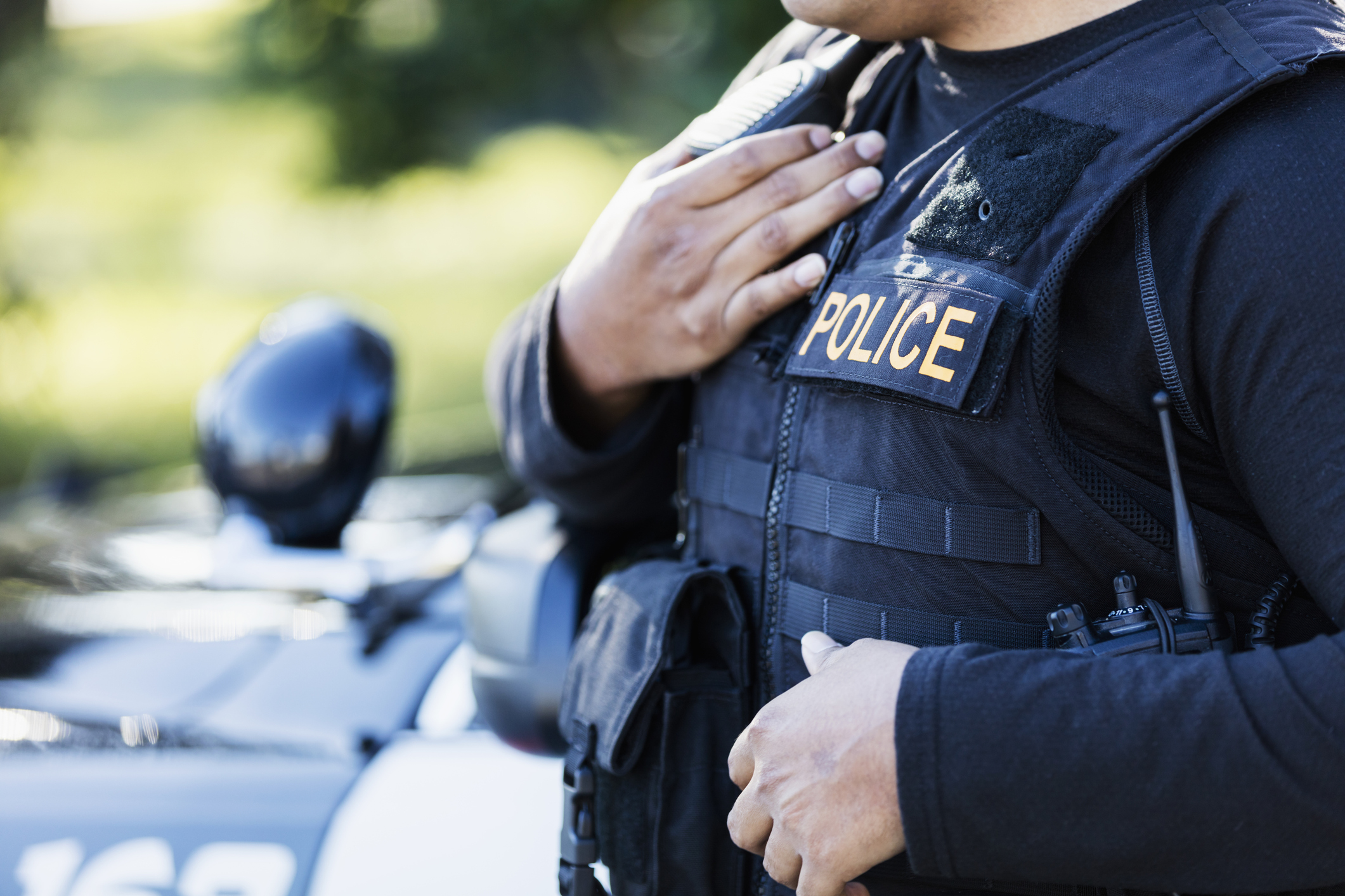 Cropped view of a young Hispanic police officer standing outside his patrol car.