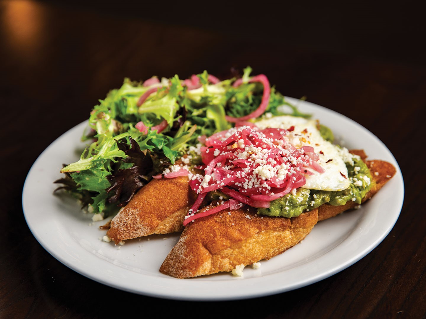 The Buttered Tin’s Smashed Avocado Toast features two slices of toasted baguette, creamy guacamole and an overeasy egg topped with Cotija cheese, crushed red pepper and pickled red onions.